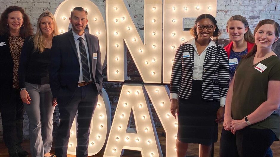 Four Teach For America alumni stand next to a One Day display